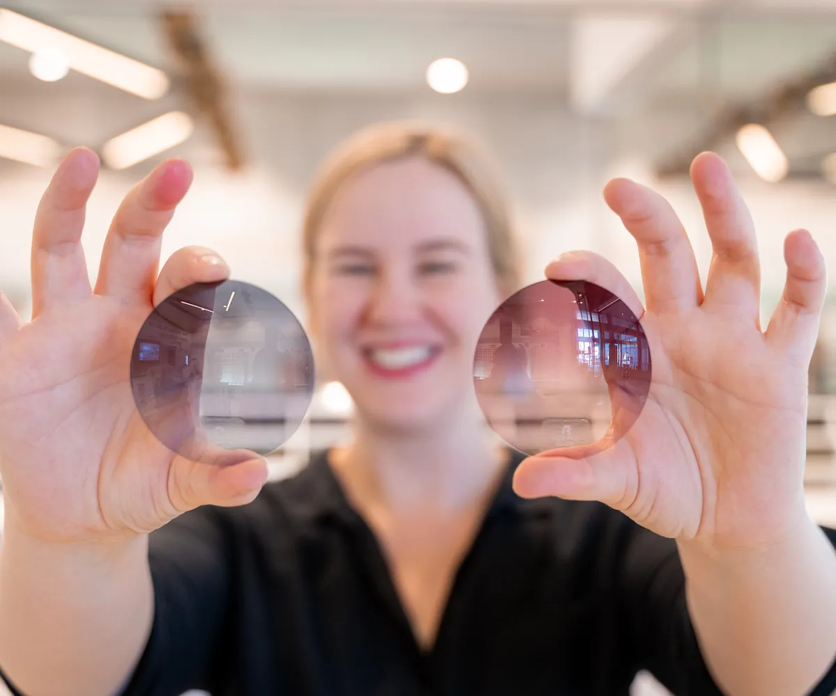 An E Eye Place team member holding up two tinted lenses of the kind used in migraine glasses, Perth